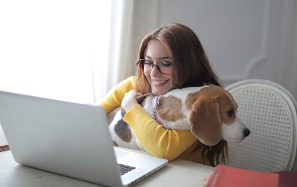 Stăpână îmbrățișând un câine beagle în fața laptopului